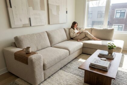 Femme lisant sur un canapé d'angle en bouclé beige dans un salon moderne avec tapis en laine et table basse en noyer