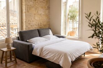 Canapé convertible déplié en lit dans un appartement marseillais avec sol en tomettes et vue sur cour méditerranéenne