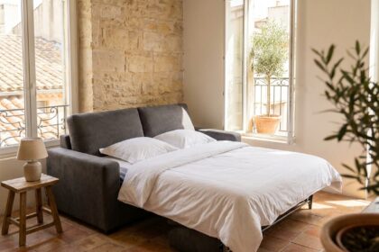 Canapé convertible déplié en lit dans un appartement marseillais avec sol en tomettes et vue sur cour méditerranéenne