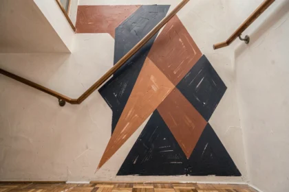 Peinture graphique géométrique bleu marine et terracotta sur le mur d'une cage d'escalier en plâtre blanc avec parquet en chêne