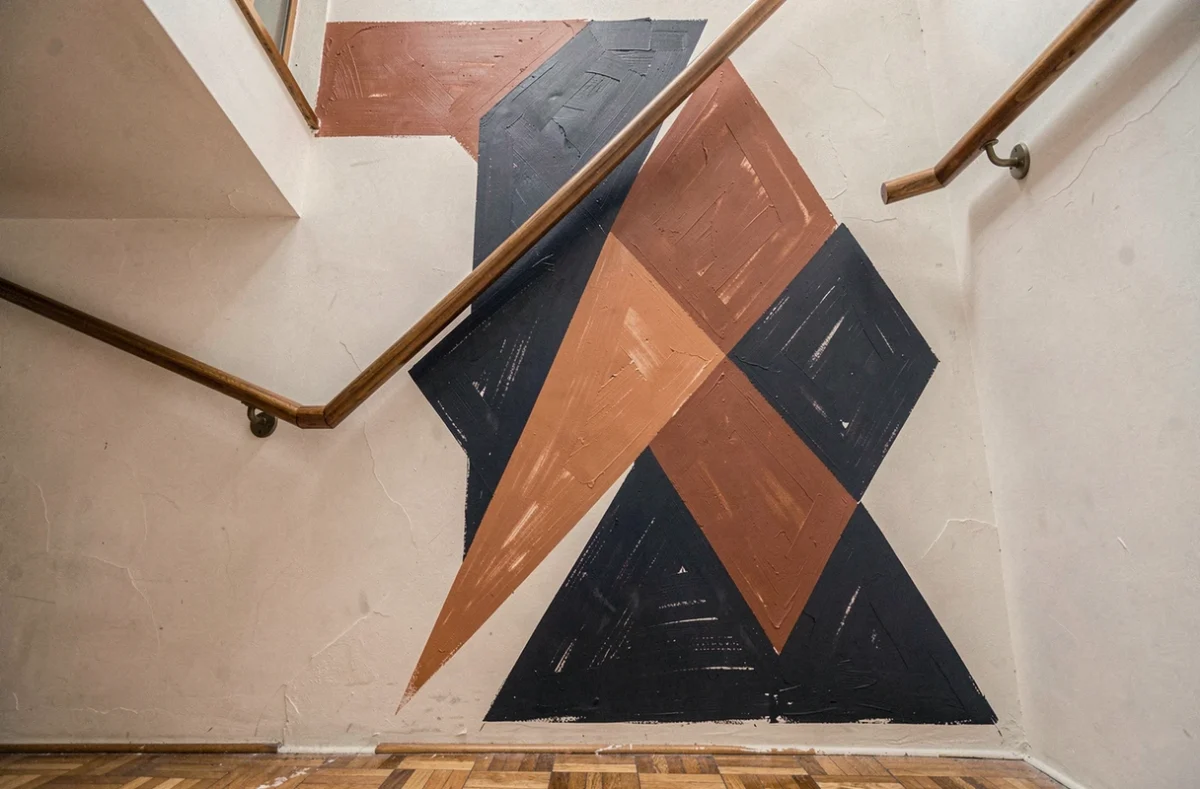 Peinture graphique géométrique bleu marine et terracotta sur le mur d'une cage d'escalier en plâtre blanc avec parquet en chêne