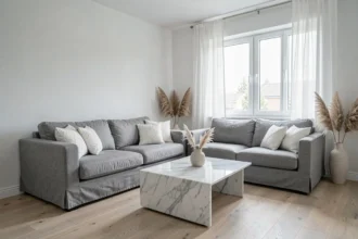 Salon moderne décoré en gris et blanc avec canapé en lin, table basse en marbre et rideaux voilages laissant entrer la lumière naturelle
