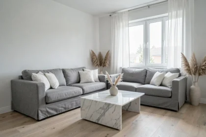 Salon moderne décoré en gris et blanc avec canapé en lin, table basse en marbre et rideaux voilages laissant entrer la lumière naturelle